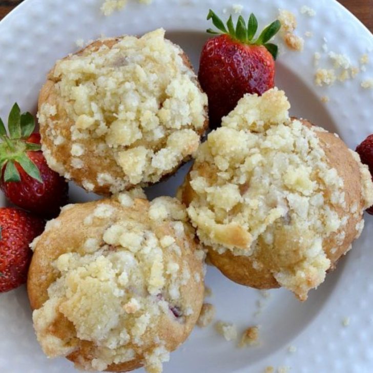 overhead view of white plate with three eggless strawberry muffins with real red strawberry off to the sides