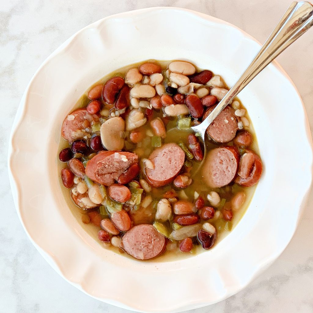closeup overhead view of Instant Pot 15 bean soup with sausage in a white bowl with spoon