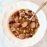 closeup overhead view of Instant Pot 15 bean soup with sausage in a white bowl with spoon