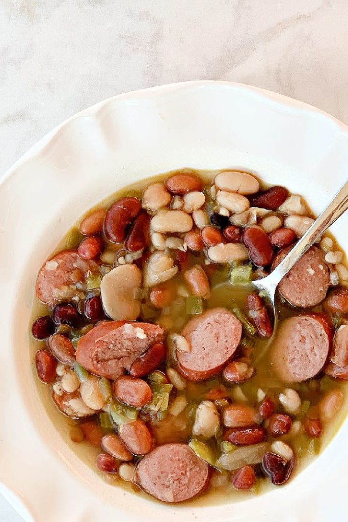 overhead view of Instant Pot 15 bean soup with sausage in a white bowl with spoon