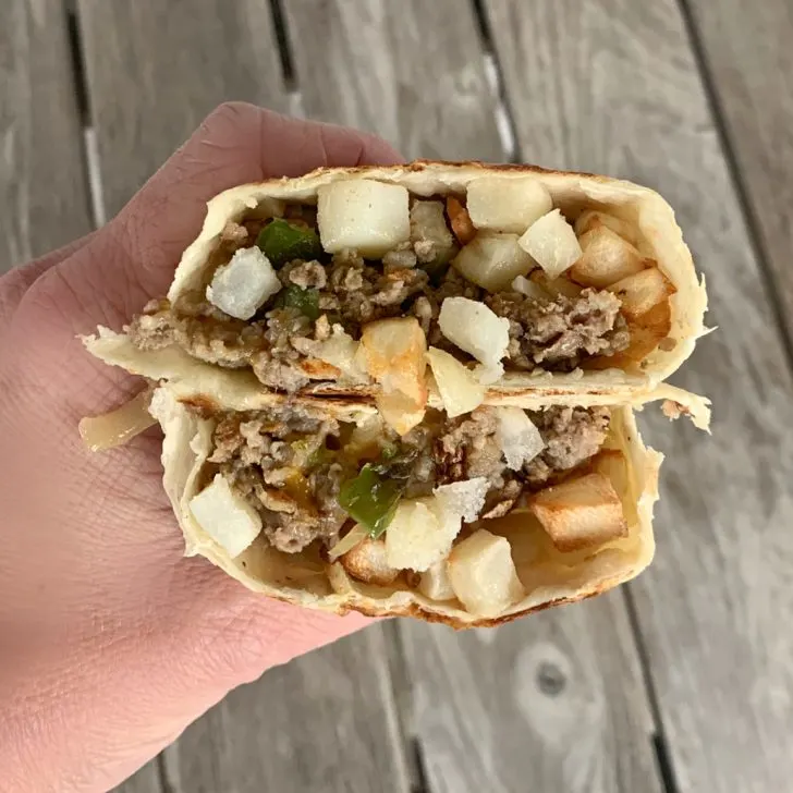 hand holding eggless breakfast burrito cut in half to see ground sausage and hash browns