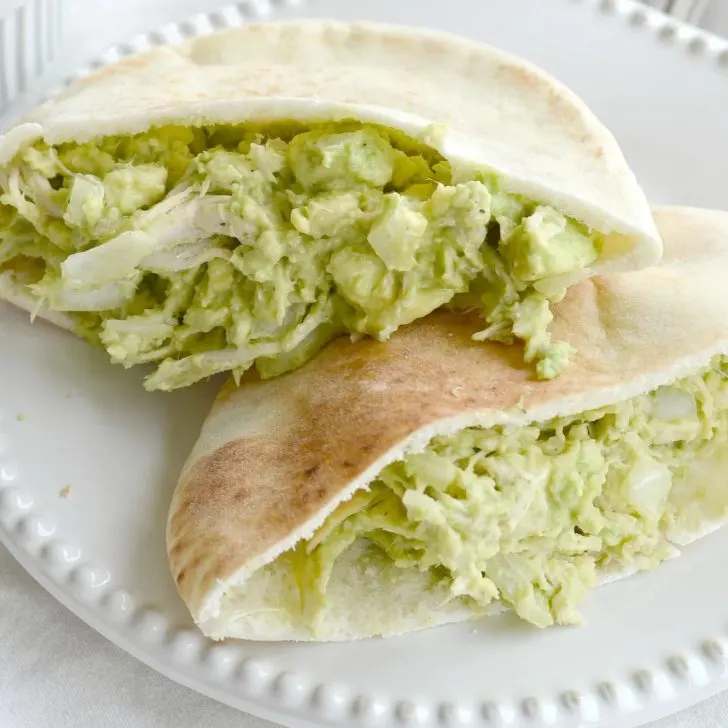 split pita bread with green chicken salad without mayo with avocados on white plate.