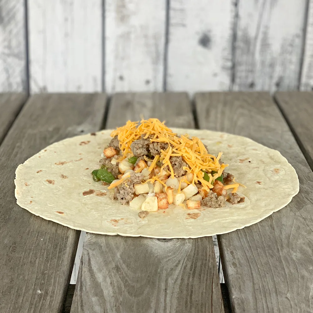 tortilla on wooden table with hash browns, ground sausage and shredded cheese