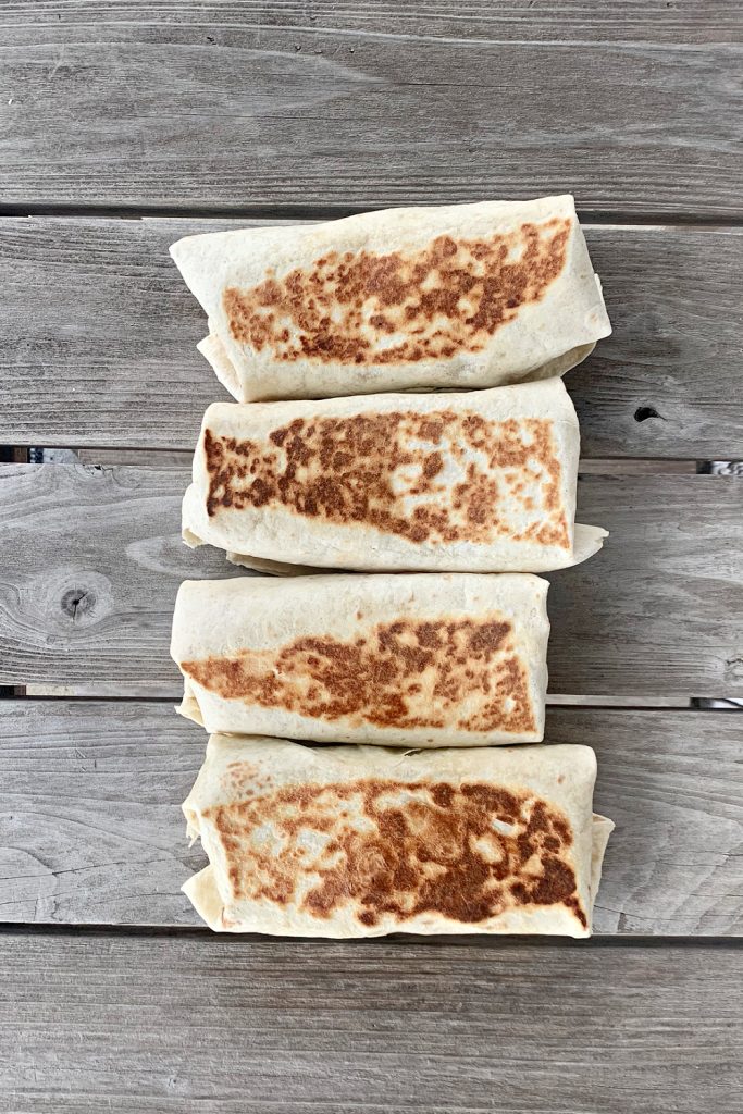 4 breakfast burritos laying in a row on a wooden table