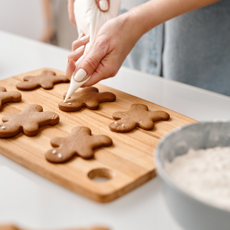 lady putting white icing on gingerbread men laying on a wooden cutting board