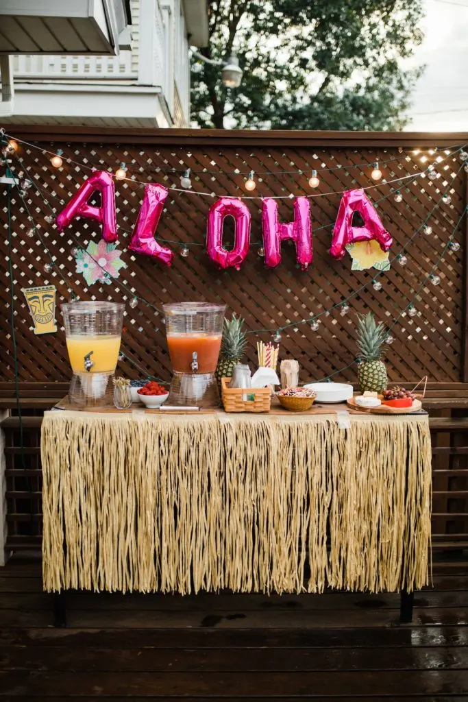 aloha themed party with grass skirt table cloth,. pink aloha balloons, punch and pineapples on the table