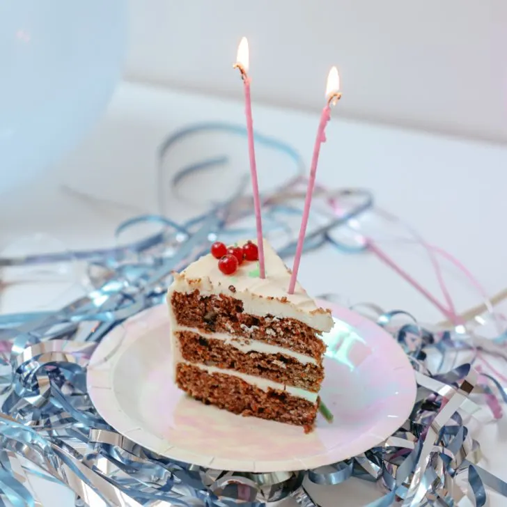 triple layer cake with white icing with two long candles on a white table with solver metallic streamers