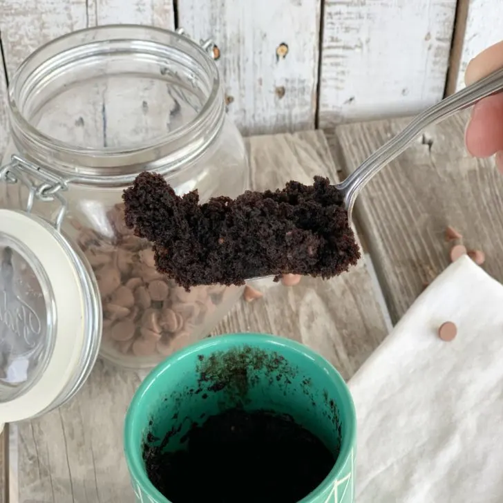 chocolate mug cake on a fork with jar with chocolate chips and green mug